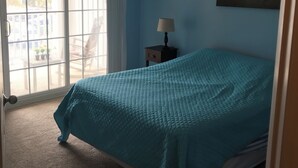 Ein Schlafzimmer mit einem Bett, einem Nachttisch, einer Lampe, einem Deckenventilator und einem Fenster mit Jalousien.