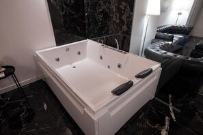 Ein modernes Badezimmer mit einer großen weißen Badewanne, schwarzen Marmorwänden und einem Ledersofa.