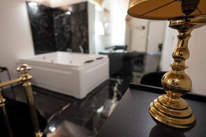 Ein modernes Badezimmer mit einer weißen Badewanne, einer Wand aus schwarzem Marmor und einer Messinglampe auf einer schwarzen Ablagefläche.