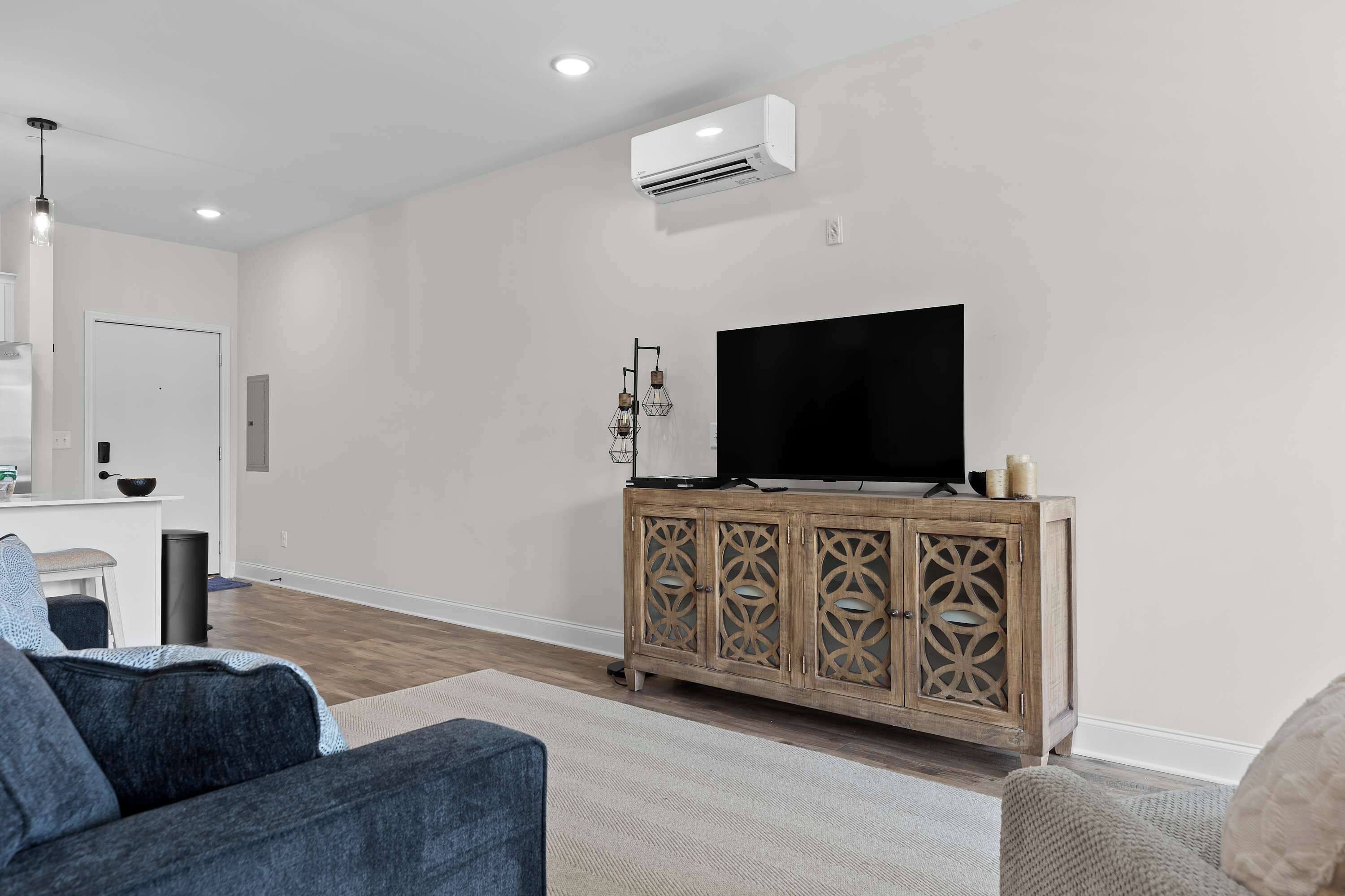 A modern living room with a flat-screen TV on a wooden cabinet, a sofa, and a dining area with a white table and chairs.