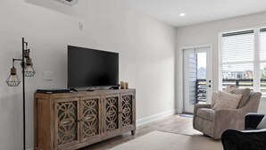 Un salon comprenant un meuble en bois, un téléviseur à écran plat, une lampe sur pied et un canapé.