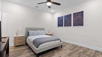 A bedroom with a bed, wooden nightstands, a ceiling fan, and abstract wall art.