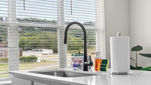 Una cocina moderna con un lavamanos de acero inoxidable, armarios blancos y una ventana con persianas.