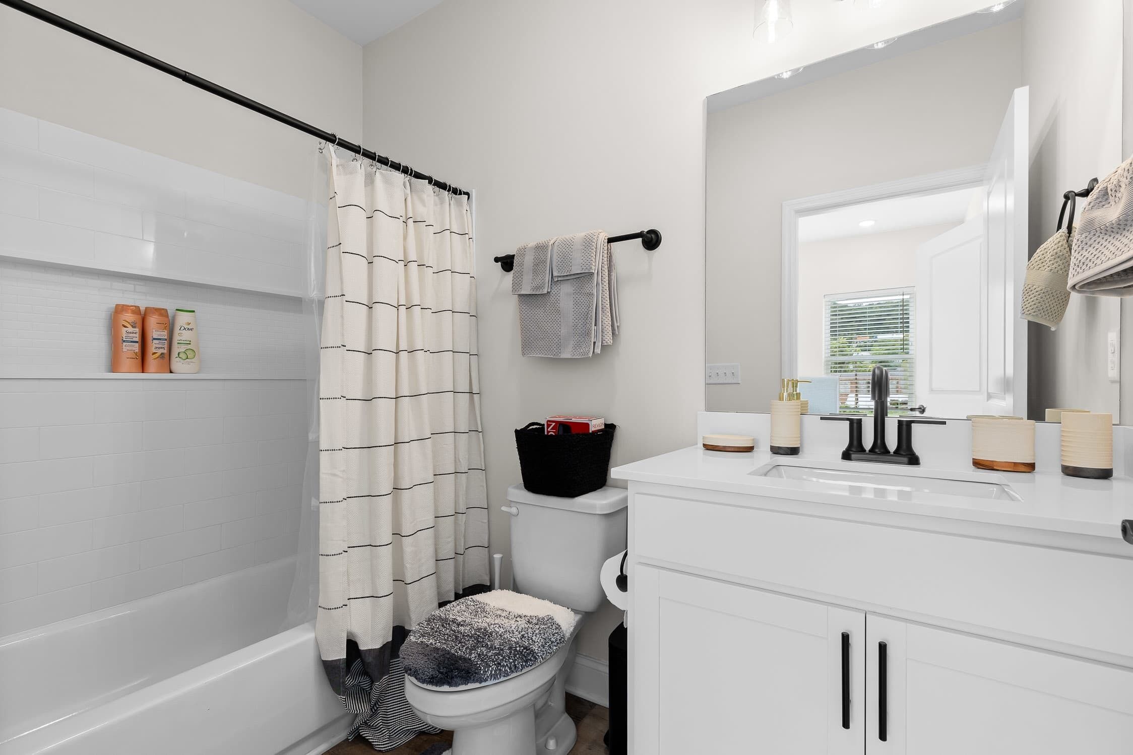 A modern bathroom with a bathtub, toilet, and sink. There are toiletries on the wall and a basket on the toilet.