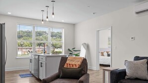 Una sala moderna con un sofá, una silla, una mesita y una zona de cocina con ventanal.