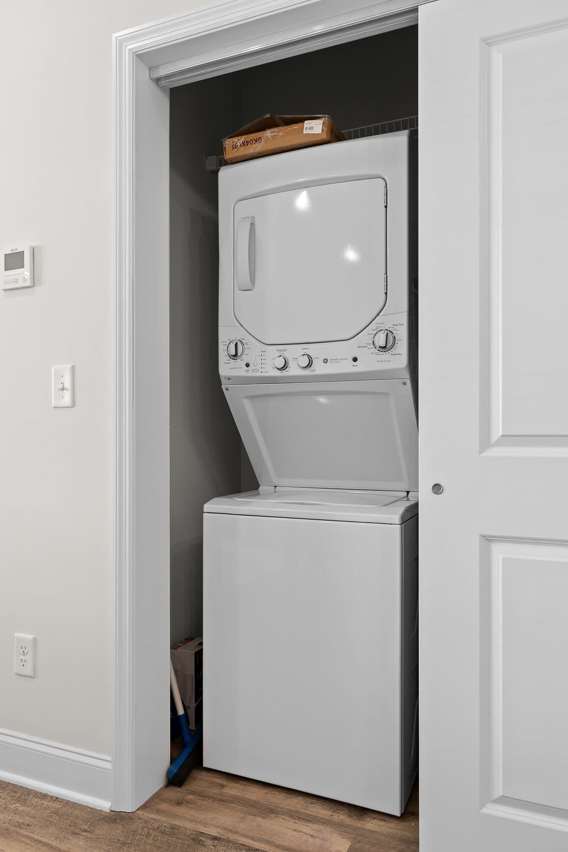 Une petite buanderie équipée d’un lave-linge et d’un sèche-linge à chargement frontal, d’une prise de courant et d’une porte donnant sur une autre pièce.