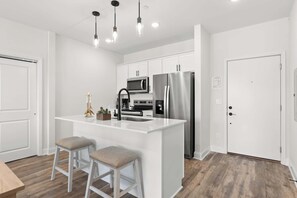 Een moderne keuken met witte kasten, roestvrijstalen apparatuur en een centraal kookeiland met krukken.