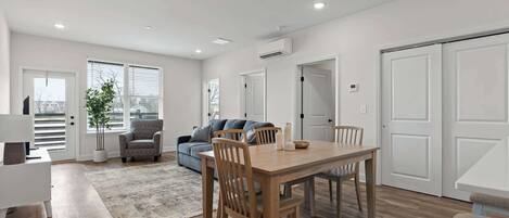 A modern living room with a dining area, featuring a wooden dining table, chairs, a sofa, and a rug.