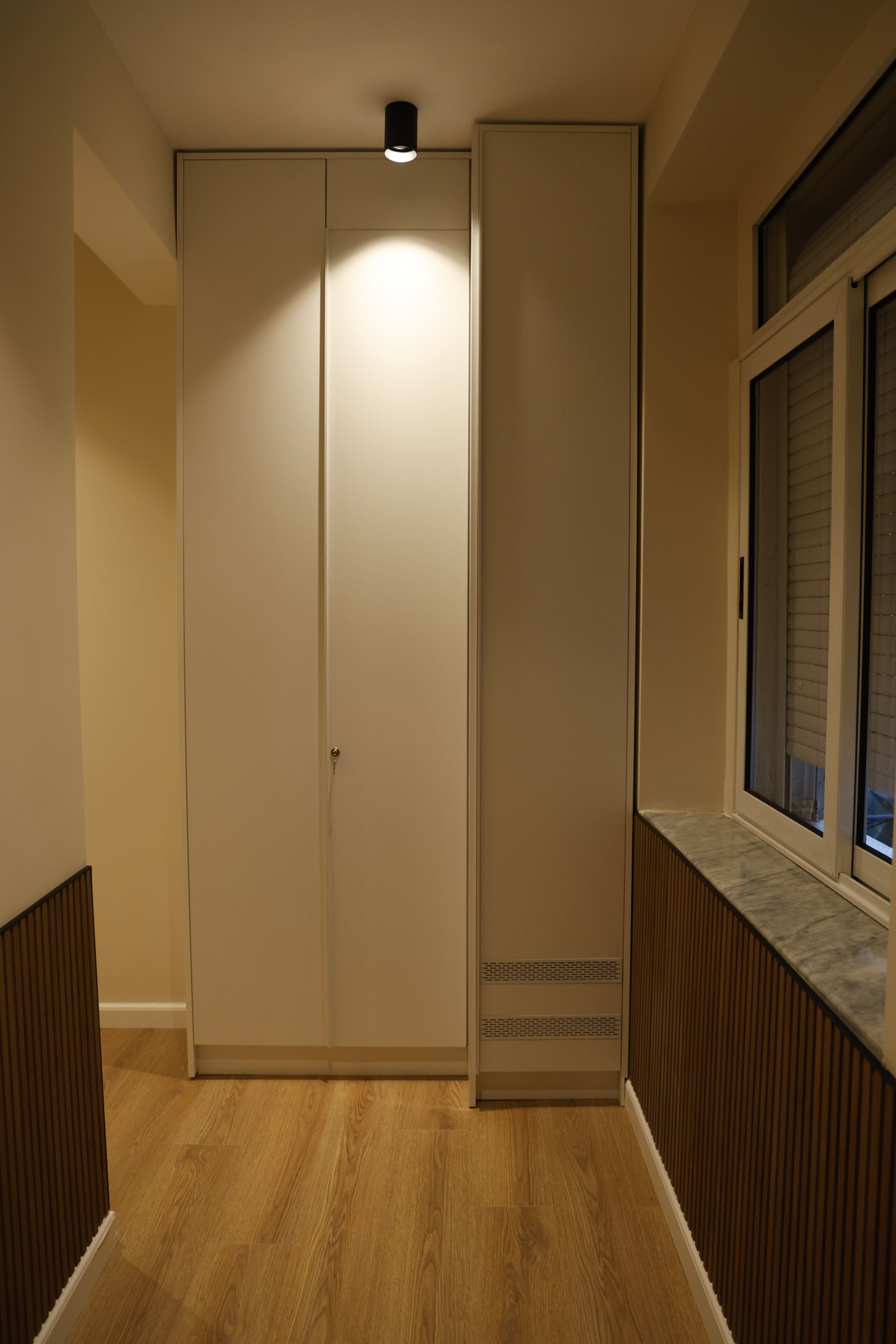 A hallway with a wooden floor, a sliding door, and a window with blinds.