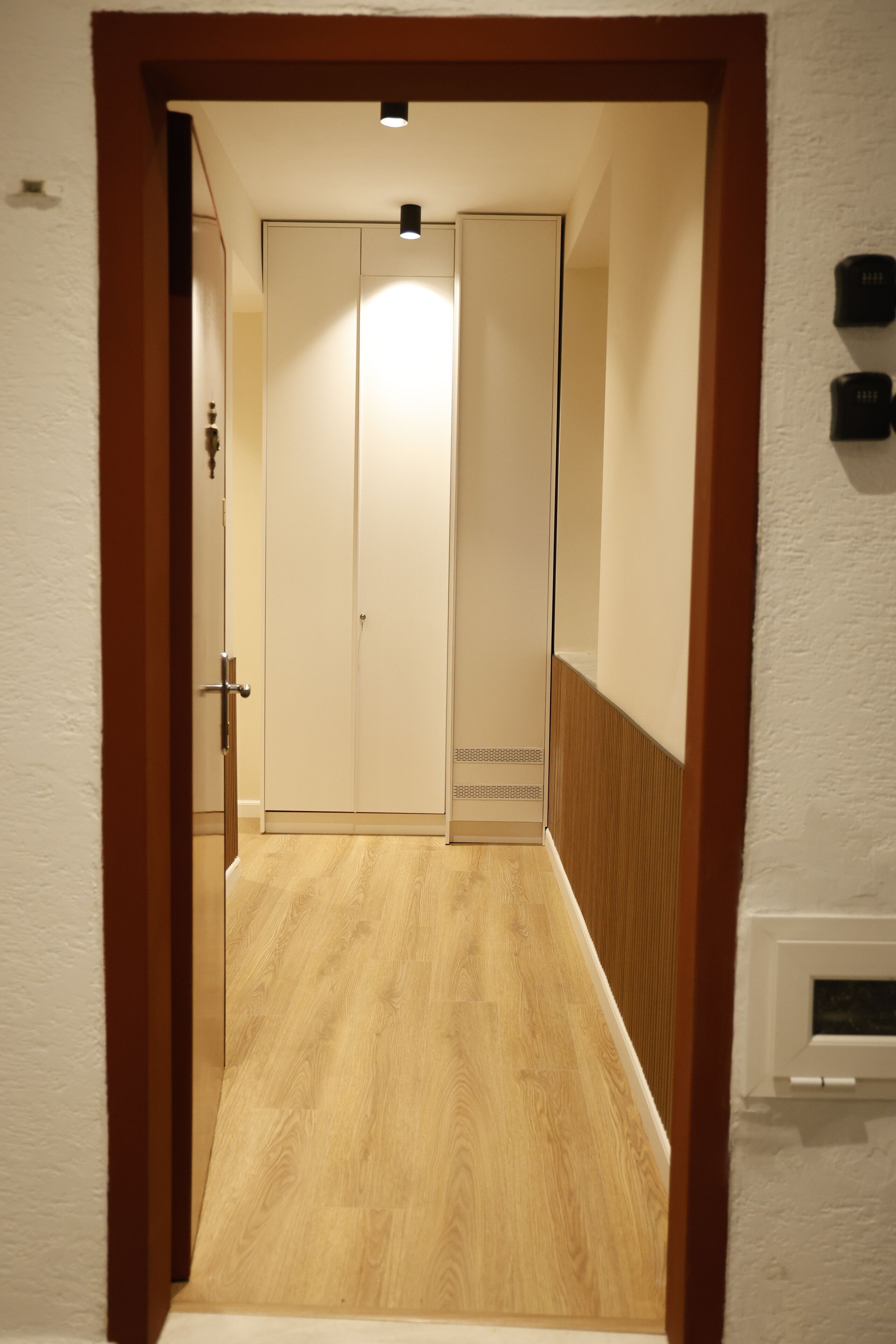 A hallway with wooden flooring, a door with a handle, and a light fixture above it.