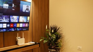 Ett modernt vardagsrum med en platt-TV som är monterad på en vägg av trä, ett runt bord, en krukväxt och en beige soffa.
