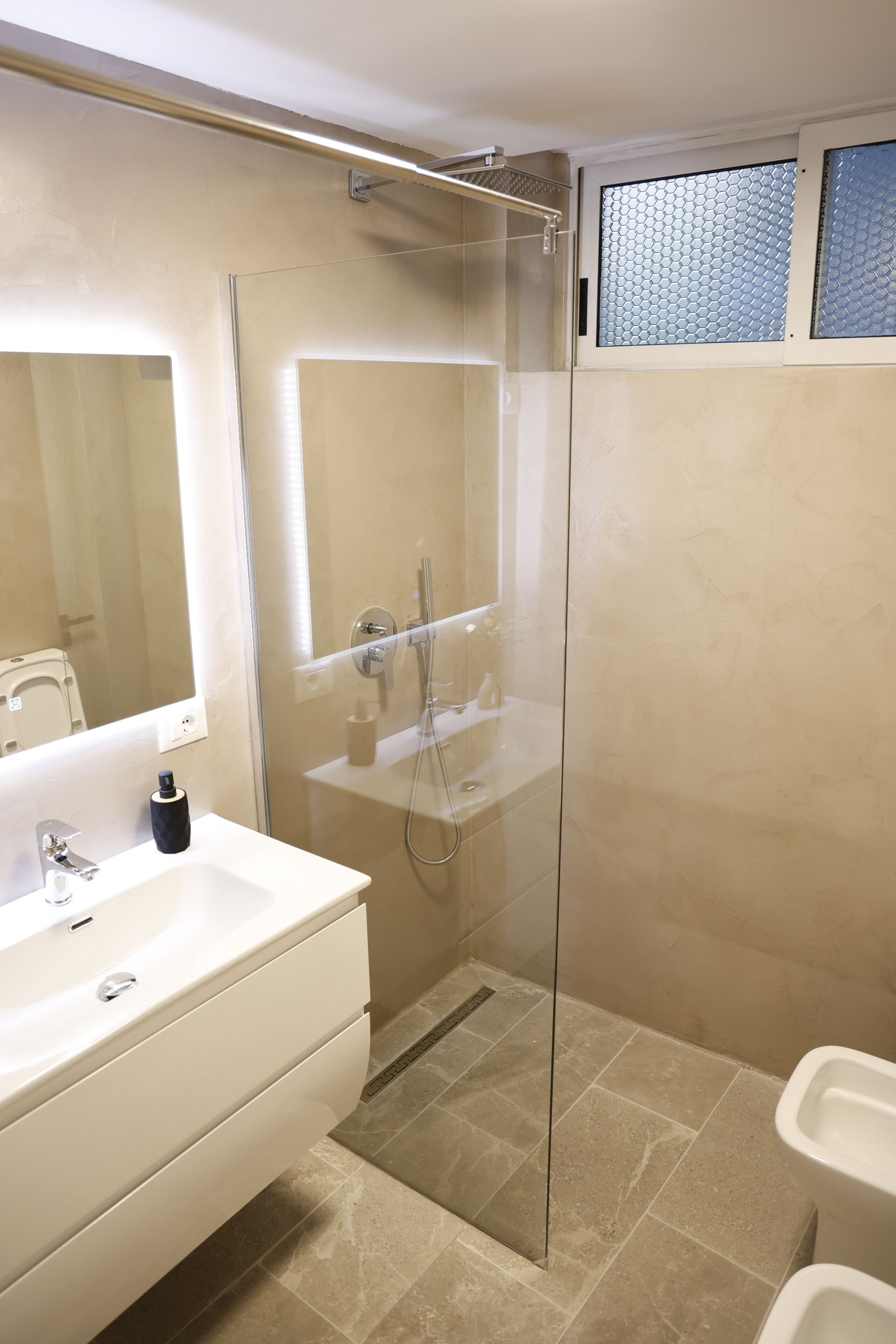 Een moderne badkamer met een douchecabine van glas, een wit wastafeltje en een spiegel.