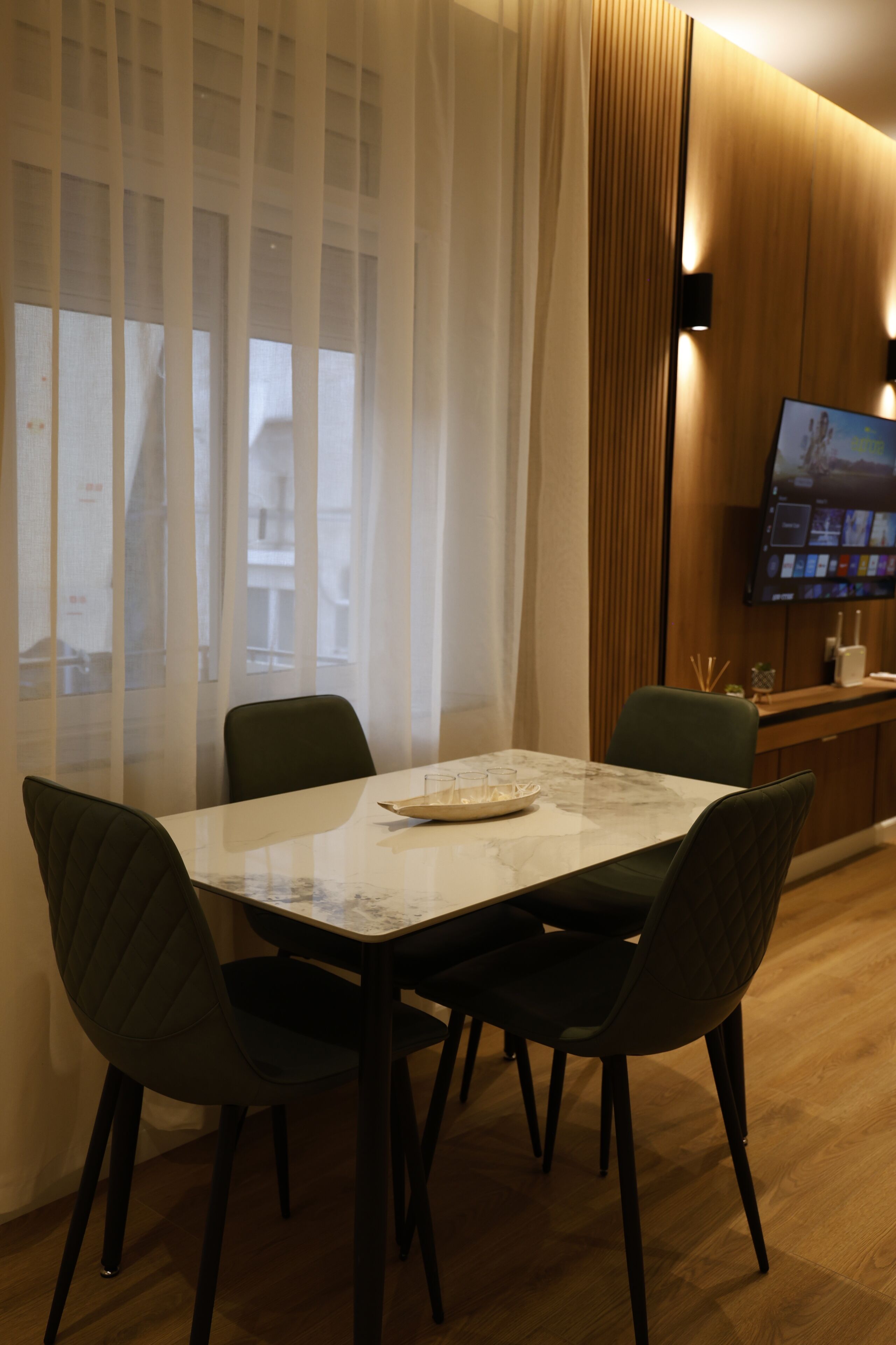 A dining area with a table, chairs, a television, and a window with curtains.