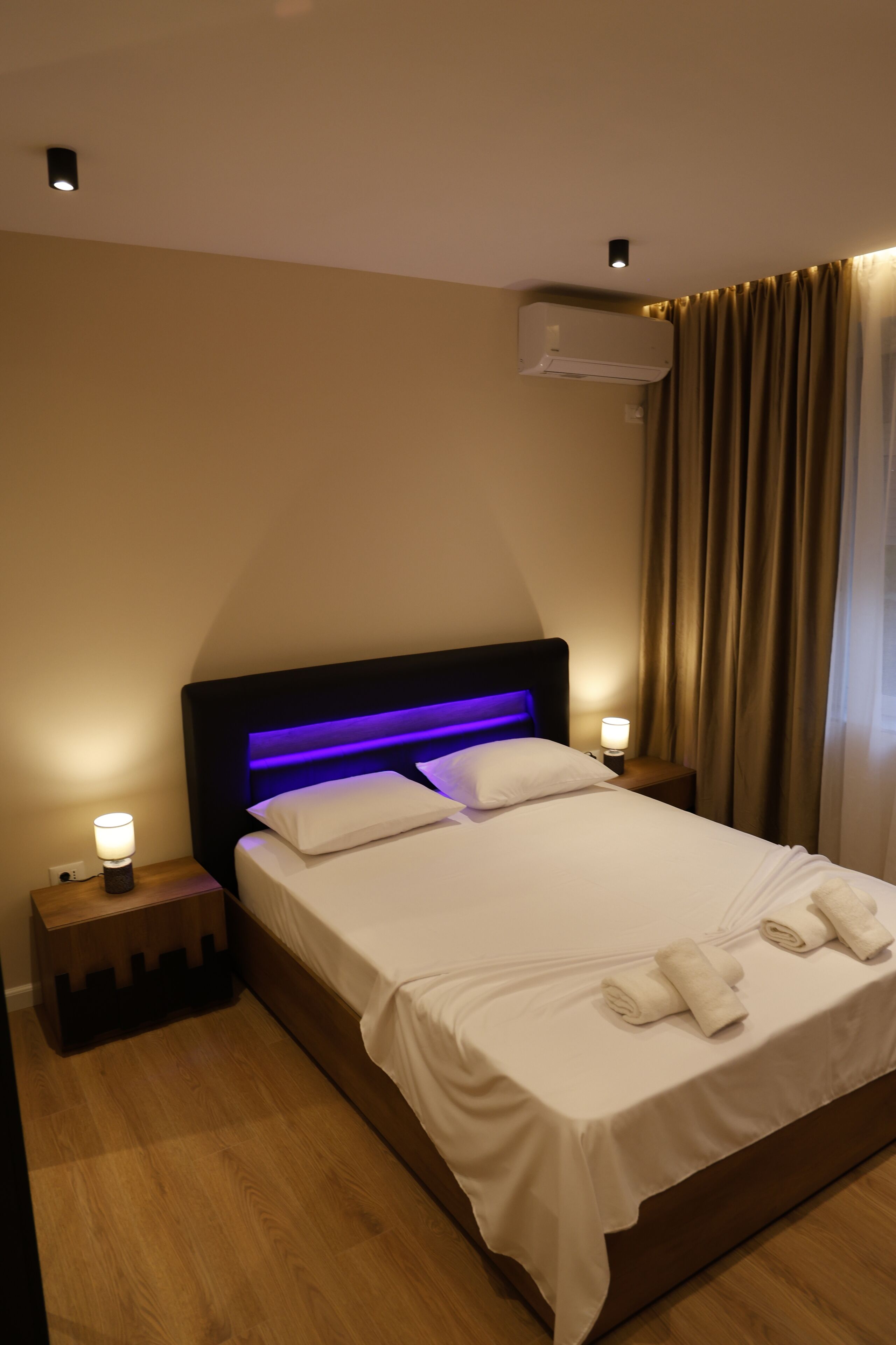 Een hotelkamer met een bed, nachtlampjes, een airconditioner en een gordijn.