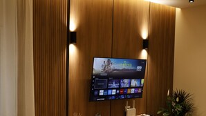 Ett modernt vardagsrum med en platt-TV som är monterad på en vägg av trä, ett litet bord med en växt och en sittgrupp med en soffa och stolar.