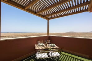 Ein Balkon mit Tisch für zwei Personen, einer Flasche und Gläsern, mit Blick auf eine Wüstenlandschaft.