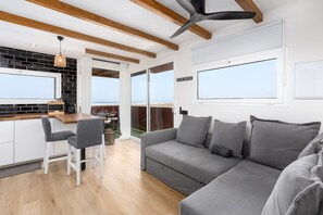Ein moderner Wohnbereich mit einer Couch, einem Esstisch mit Stühlen, einer Küchenzeile und einem großen Fenster mit Blick.