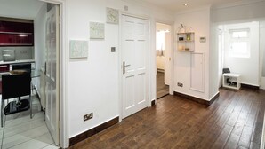 Un pasillo con suelo de madera, paredes blancas y una zona de cocina con refrigerador y armarios.