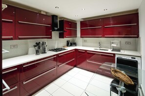 Una cocina moderna con armarios rojos, encimeras blancas y electrodomésticos de acero inoxidable.