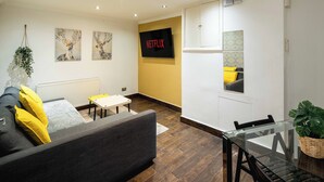 Un salón moderno con un sofá, una mesa de vidrio y un televisor mostrando 'NETFLIX'.