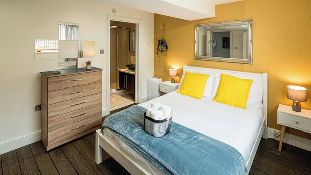 Una habitación de hotel con una cama, un tocador, una mesita de noche, un espejo y una puerta que da a un baño.