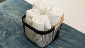 Una cesta de malla negra con asas de madera que contiene toallas blancas dobladas con cuidado.