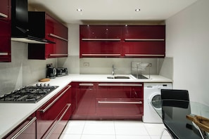 Una cocina moderna con armarios rojos, una estufa a gas, una cafetera, una lavadora y una mesa de vidrio.