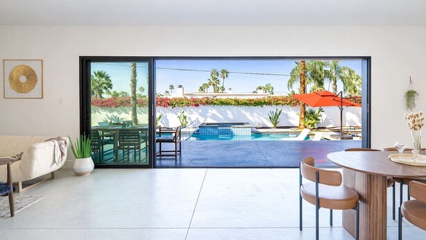A modern living room with a large sliding glass door leading to a pool area, a dining table, and a sofa. - Modern Villa|Palm Desert|Great location|Pool|Spa (Palm Desert)