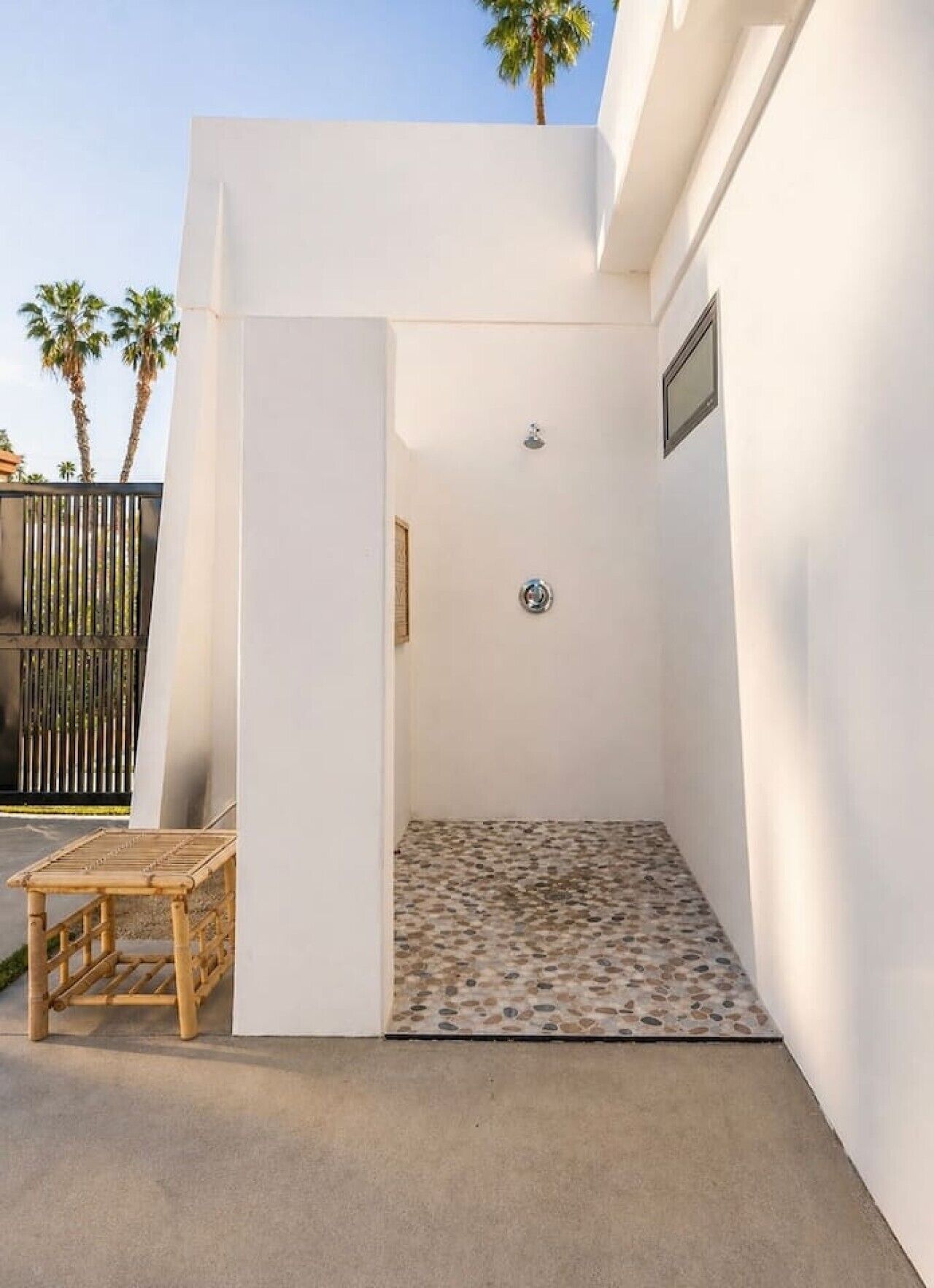 A small, enclosed outdoor shower area with a tiled floor, a wooden bench, and a metal showerhead.