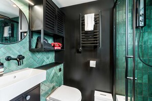 Un baño con lavamanos blanco, inodoro, toallero, espejo y zona de ducha.
