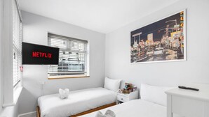 Ett hotellrum med två sängar, ett skrivbord, en tv som visar ”NETFLIX” och en affisch med en stadsbild.