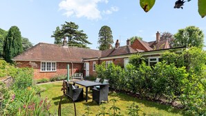 A brick house with a garden, a patio with furniture, and a large tree.