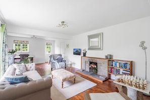 Ein Wohnzimmer mit Sofa, Hocker, Kamin, Bücherregal und einem Schachspiel.