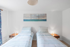 Ein Schlafzimmer mit zwei Betten, einem an der Wand hängenden Kunstwerk, Nachttischlampen und einem Vorhang.