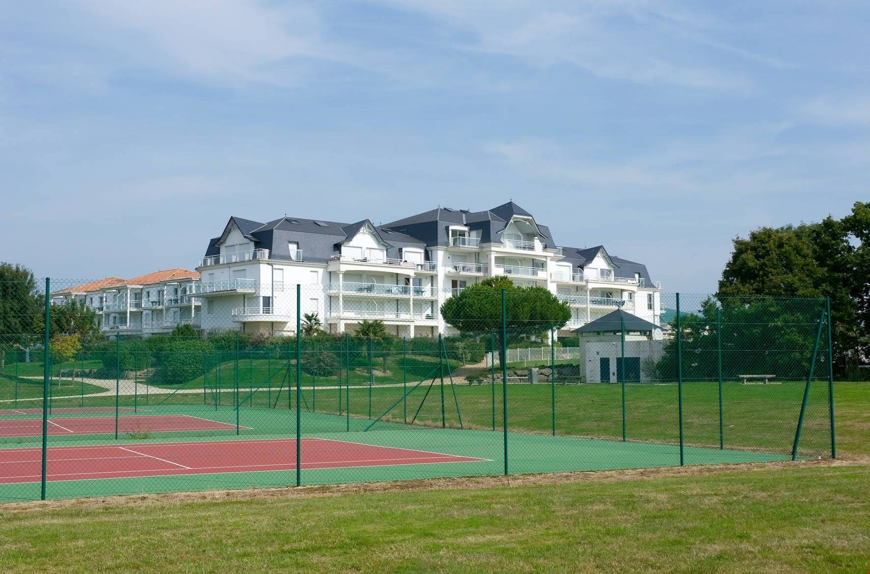 A multi-story hotel with balconies, a tennis court, and a small building in the foreground.