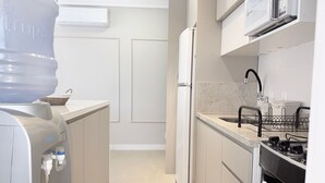 A compact kitchen with a water dispenser, a refrigerator, a microwave, a sink, and a stove.