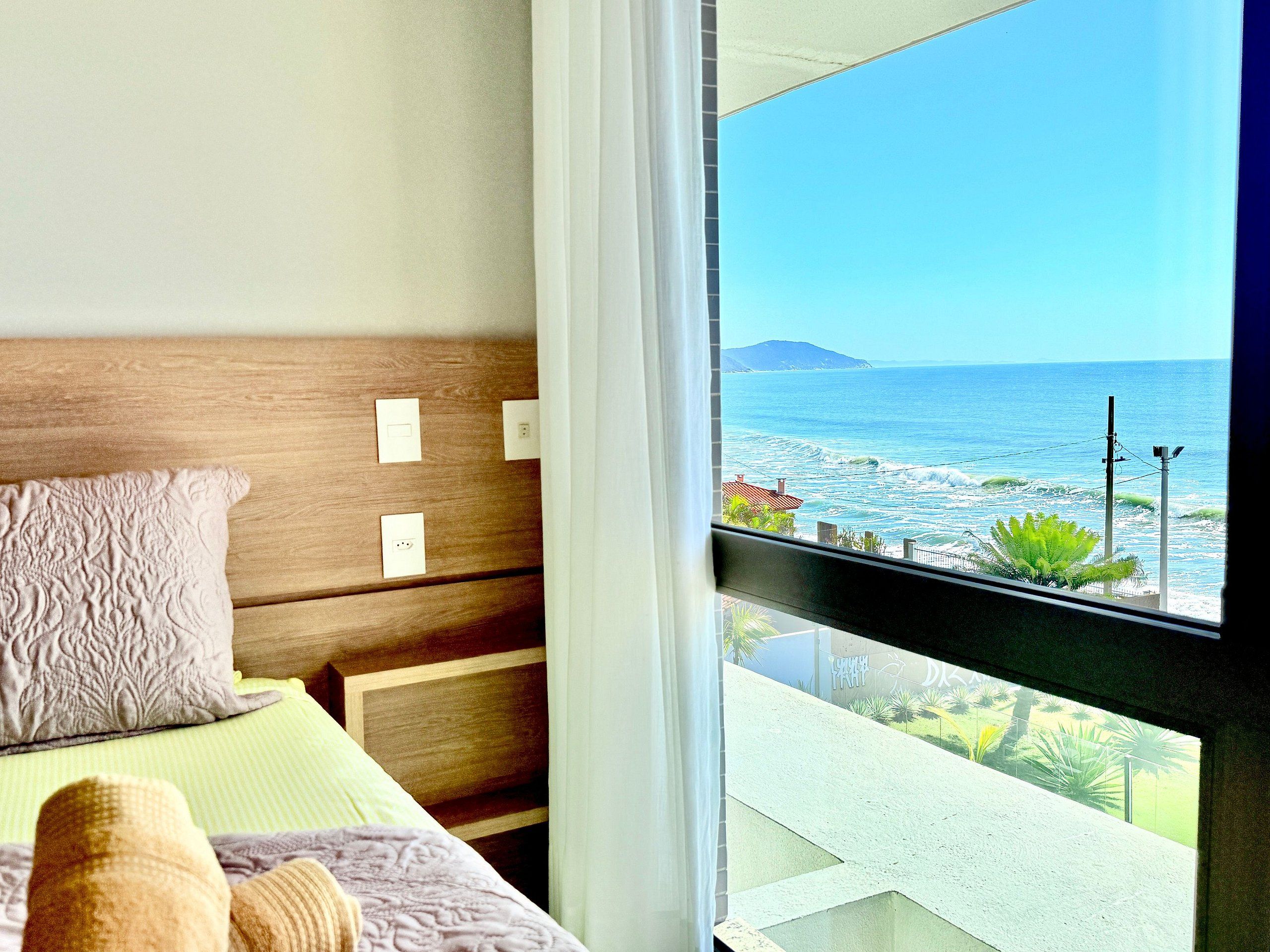 A bedroom with a wooden headboard, a bed with a patterned pillow, and a view of the ocean through a window.