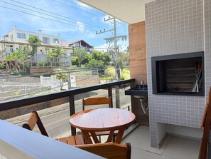 Un balcón con una mesa y sillas de madera redonda, un lavamanos negro y una pared con azulejos y una parrilla.