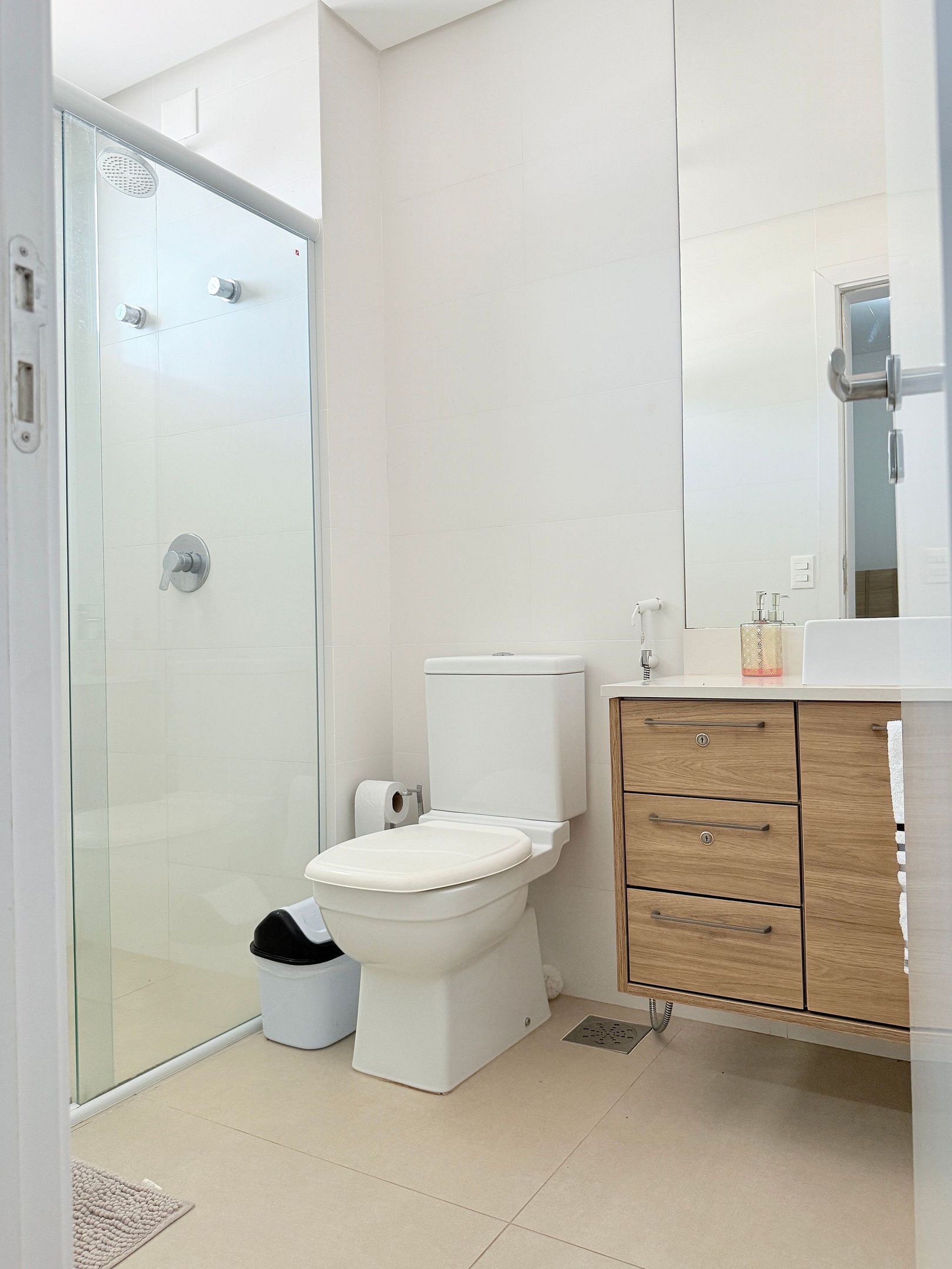 A bathroom with a glass shower enclosure, a toilet, a wooden cabinet, and a sink with a mirror above it.