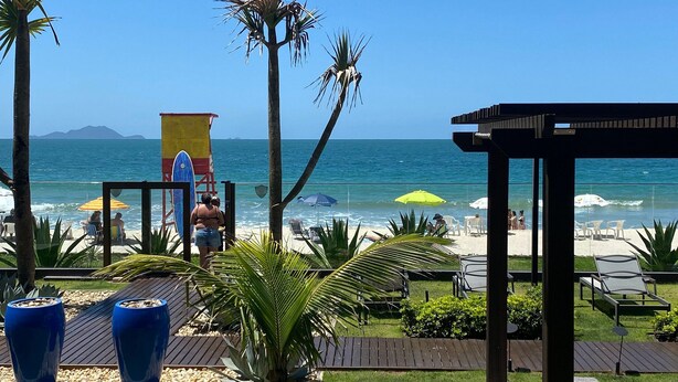 A beachside view with palm trees, a lifeguard tower, and beach chairs. - Res Belvedere Beach Garden (Florianópolis)