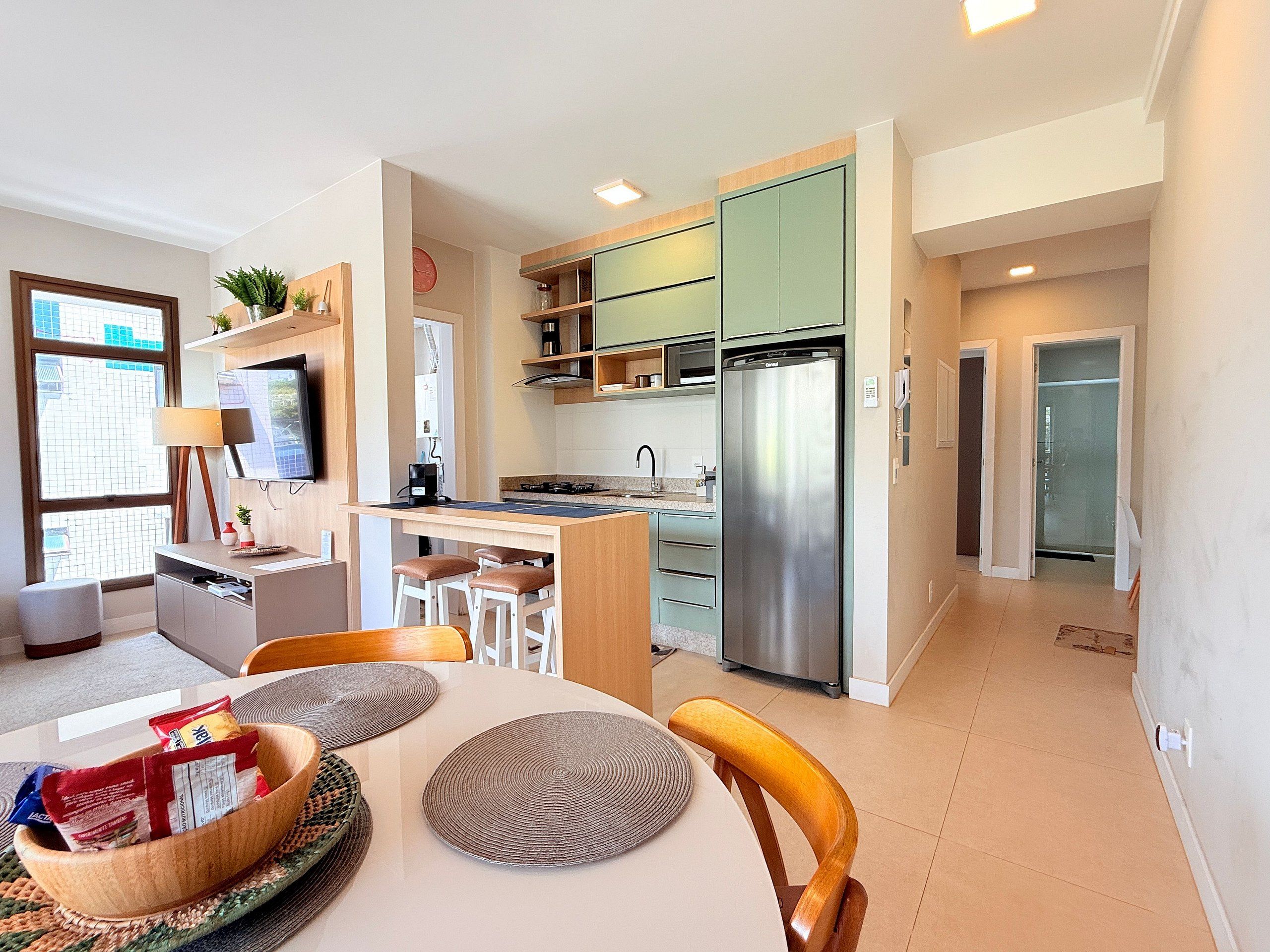 A modern kitchen with a built-in refrigerator, a dining area with a table and chairs, and a view of the city through a large window.