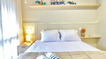 Habitación de hotel con cama, mesita de noche con lámpara, repisa con objetos decorativos y letrero en la pared.