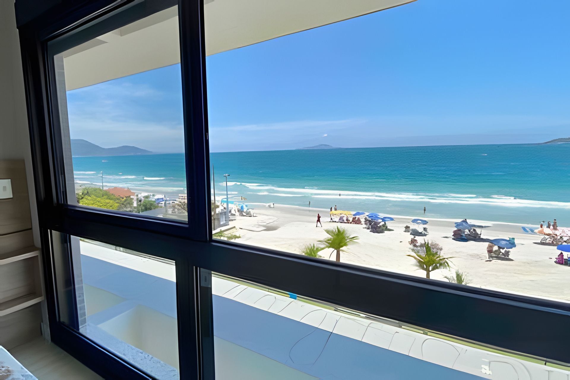 A view of a beach with umbrellas and people, a clear sky, and a distant mountain.