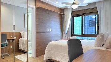 A hotel room with a bed, a desk, a chair, a ceiling fan, and a window with a city view.