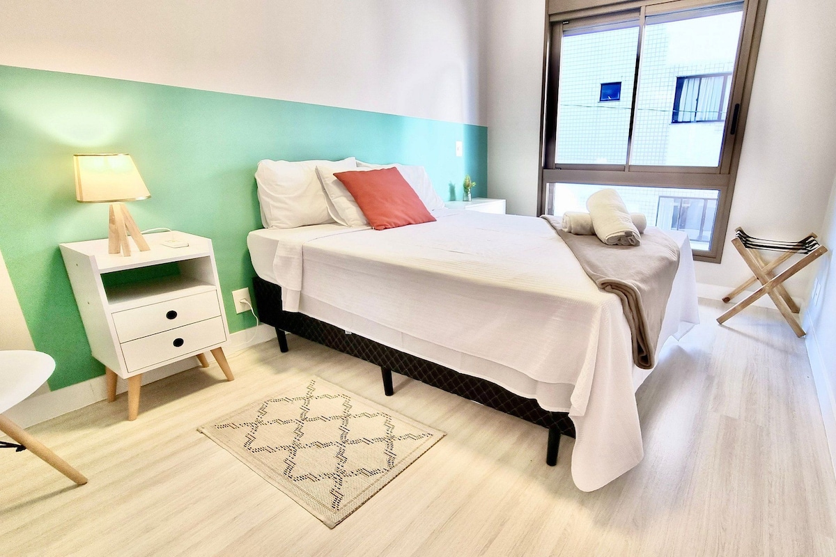 Une chambre à coucher bien rangée, avec un lit, une table de chevet, une lampe et une vue sur l’extérieur par une fenêtre.