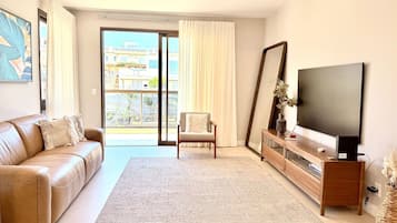 A modern living room with a leather sofa, a wooden coffee table, a flat-screen TV, and a large window with curtains.