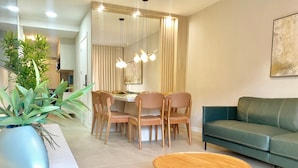 A modern living room with a green sofa, wooden dining table, and chairs, a small round table, and a potted plant.