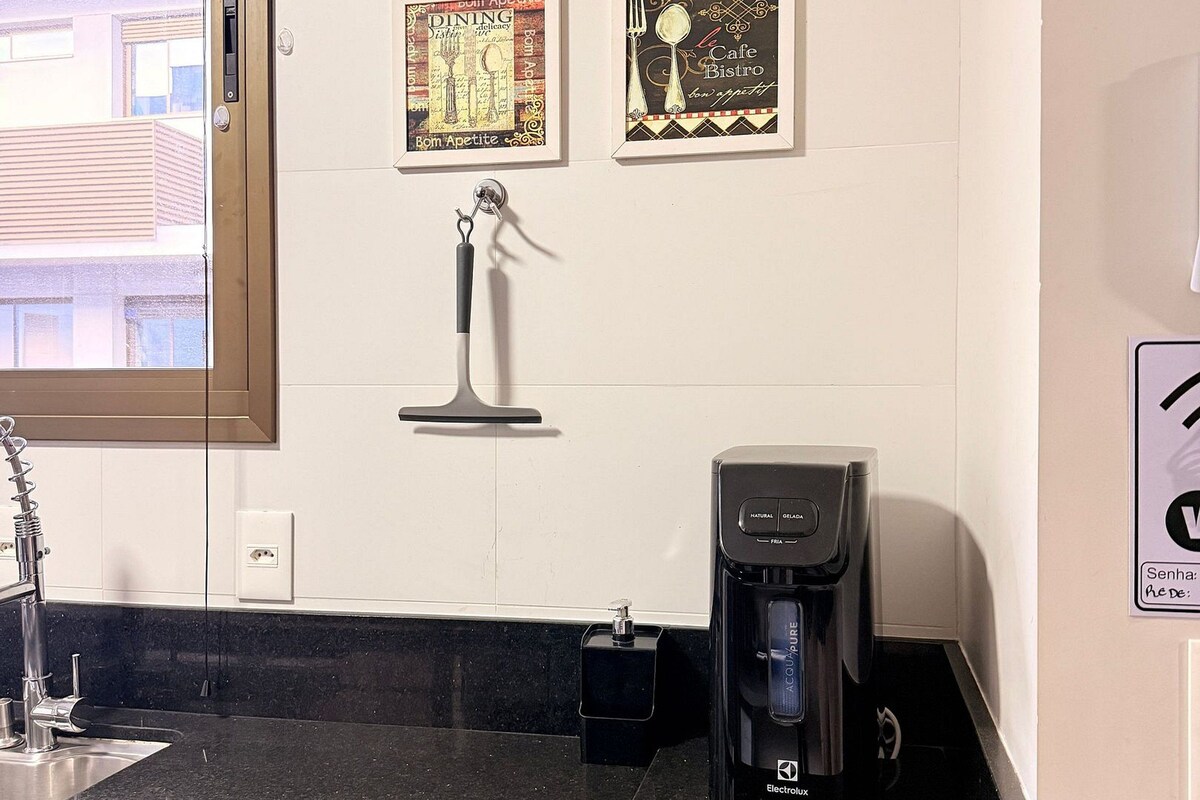 Ett kök med en svart bänkskiva, en kaffebryggare och fyra inramade tavlor på väggen.