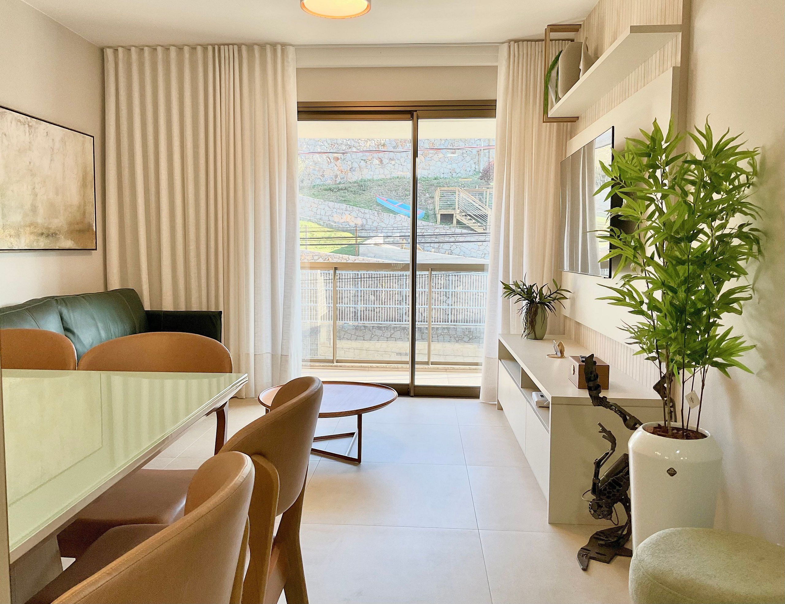 A modern living room with a dining area, a large window with a view of a stone building, and a potted plant on the right.