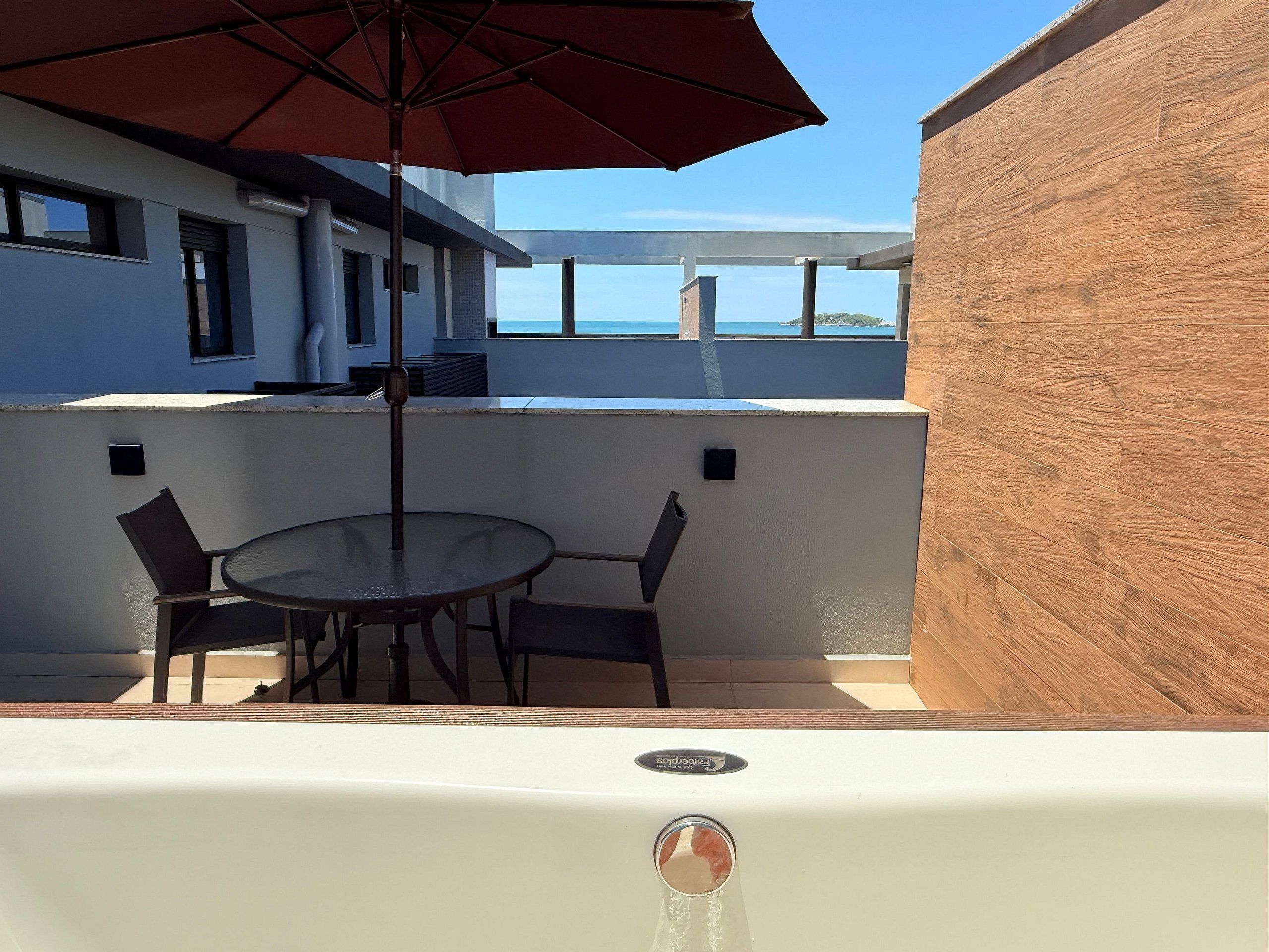 Una terraza con mesa y sillas, una sombrilla y vista al mar.